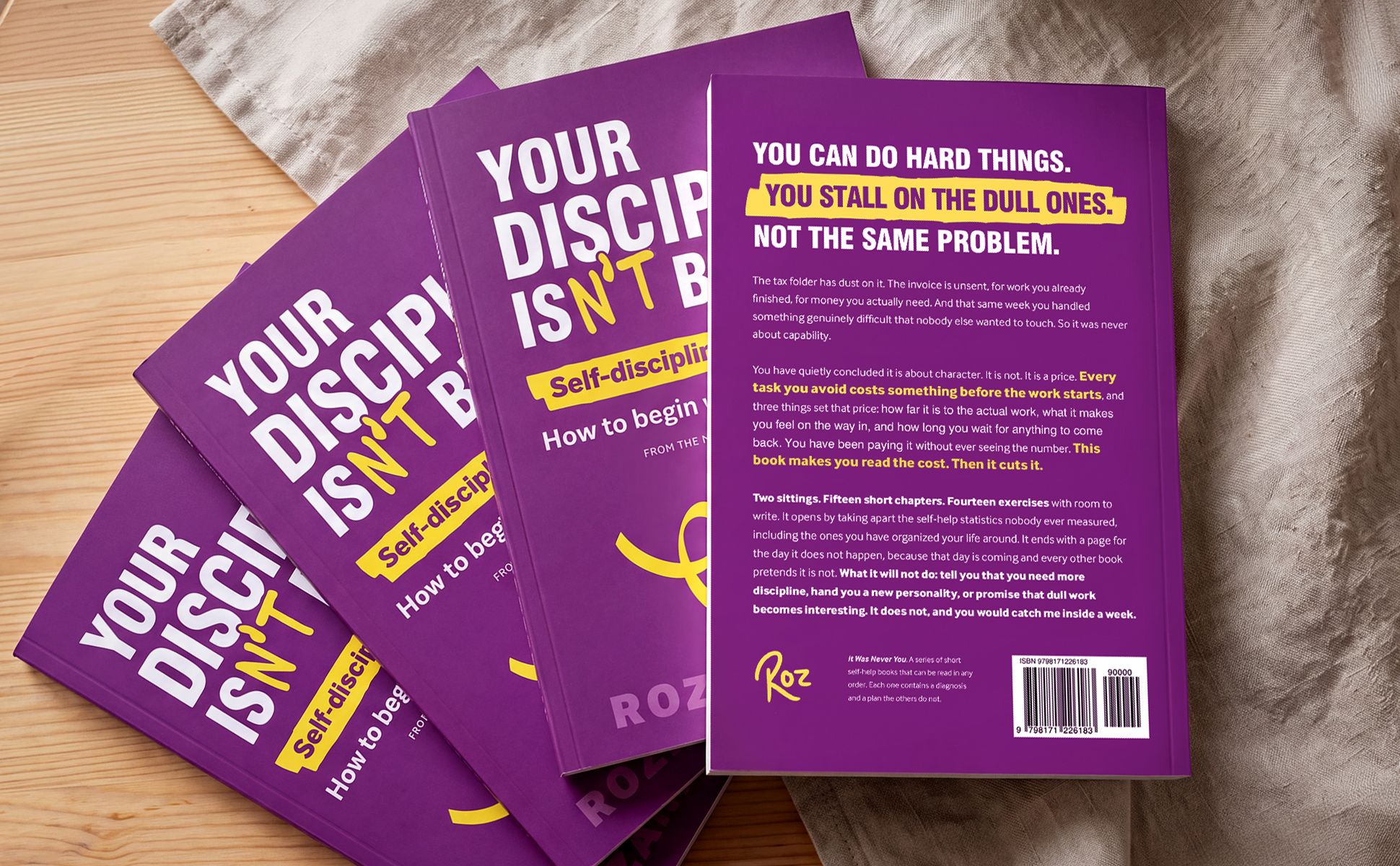 Four copies of the paperback fanned out on a wooden table, the top one turned over to show the back cover and its three-line headline on purple.